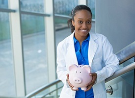 smiling dentist holding a pink piggy bank