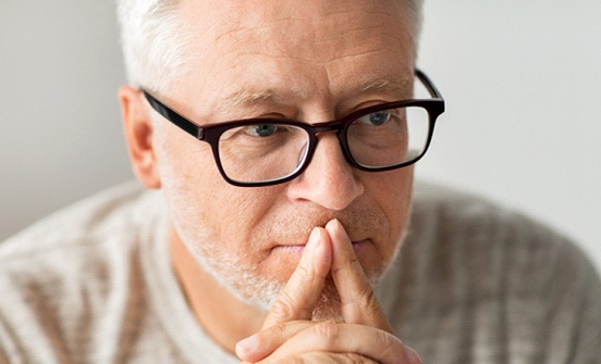 A middle-aged man wearing glasses and thinking about his decision to pursue dental implants in Clinton Township