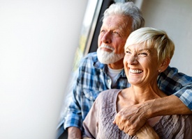 An older couple staring out a window and smiling after receiving their new dental implants