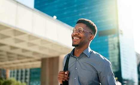 a smiling man with glasses with a high-rise building in the background
