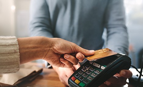 a hand holding their credit card up to a payment pad
