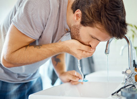 a man rinsing his mouth using a bathroom sink