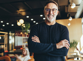 a man wearing glasses and smiling with his arms crossed