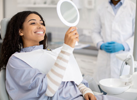 a woman looking at her smile in a handheld mirror at a dental office