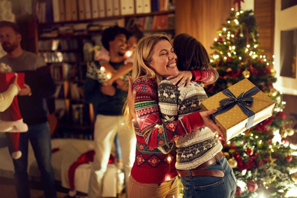 Woman hugging while exchanging presents by the Christmas tree