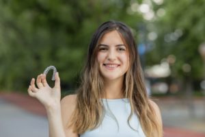 Smiling woman holding Invisalign while outside