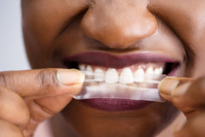 a person placing a whitening strip on their teeth