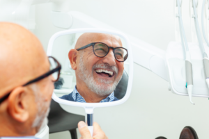 a smiling man looking in a handheld mirror